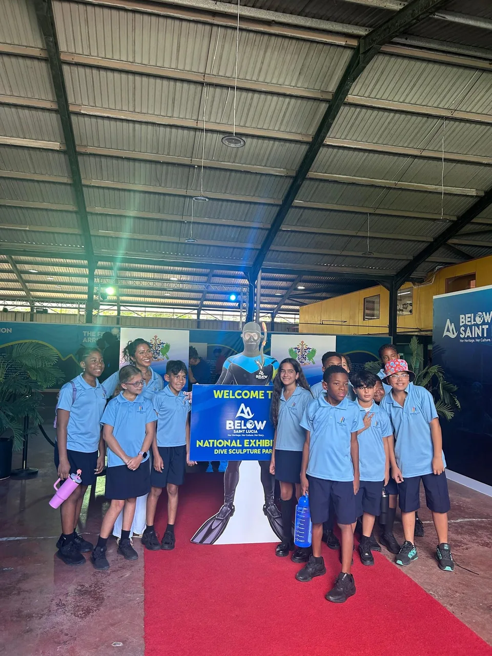 Older students stand on the red carpet beside a diver cut-out and the exhibition welcome sign