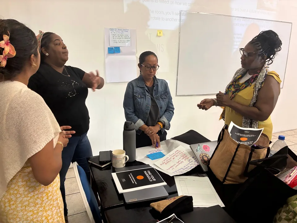Four staff members talk together around a table of papers in front of a whiteboard