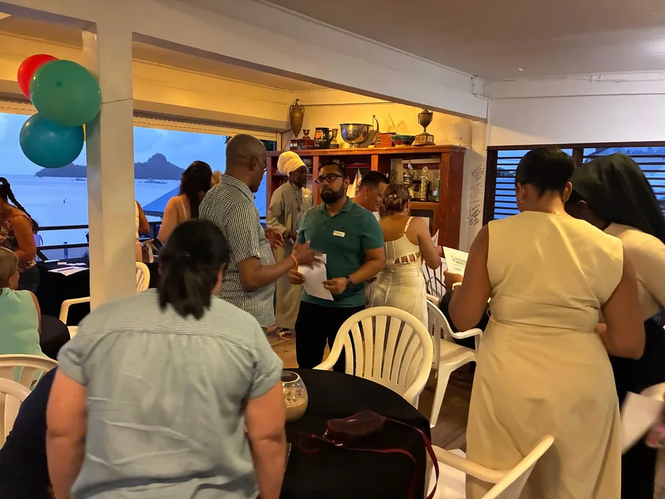 Parents and staff stand chatting in a room with balloons and a sea view behind them