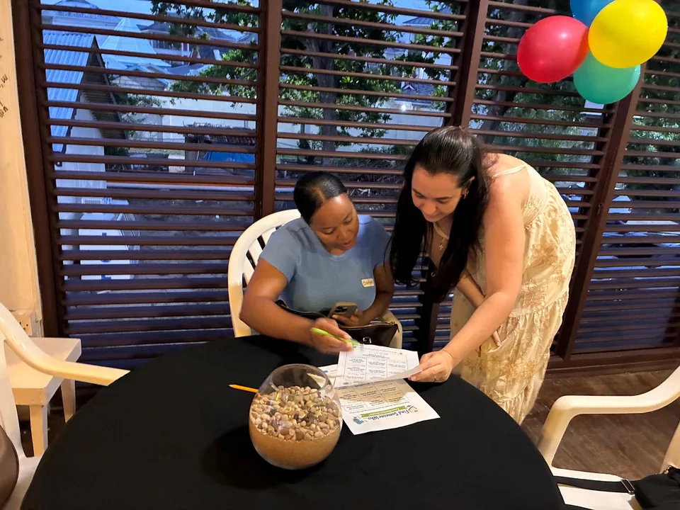 A woman leans over to point at a form as a staff member fills it in at a table