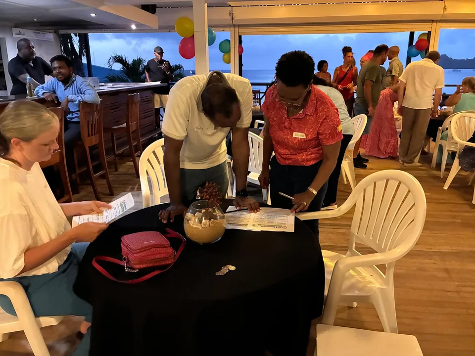 A parent and staff member lean over a table to fill in forms at dusk by the sea