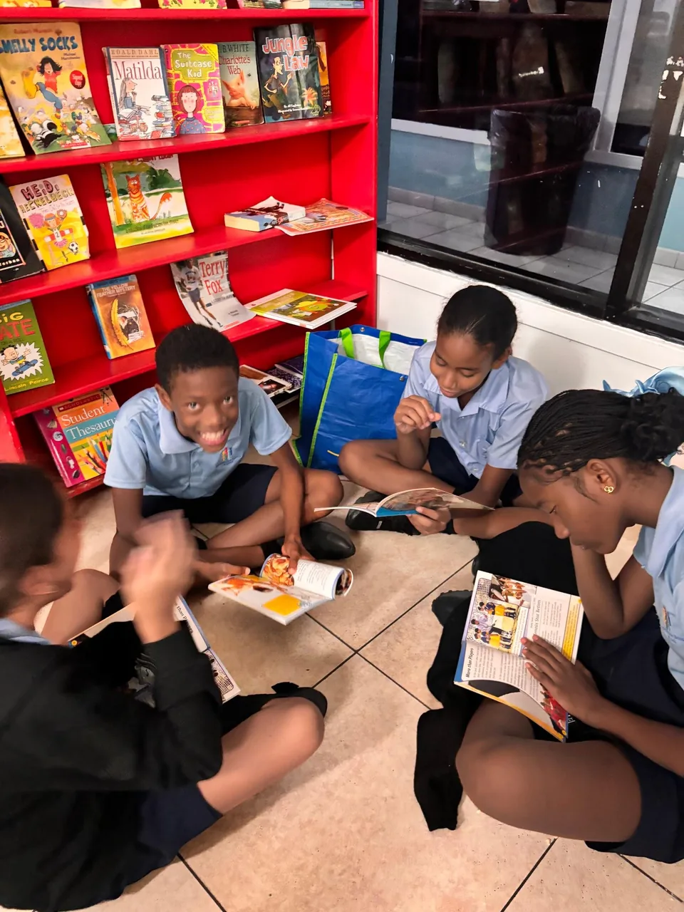 Students sit on the floor reading books in front of a red bookshelf