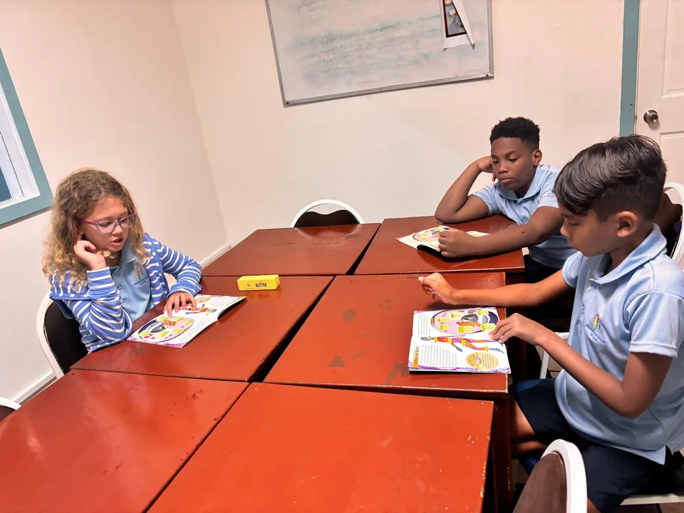 Three students read booklets around red classroom tables