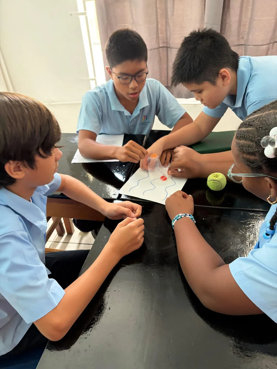 Students gather around a table working on a paper activity with wavy lines