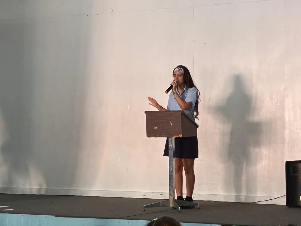 A student gestures while speaking into a microphone at the stage lectern