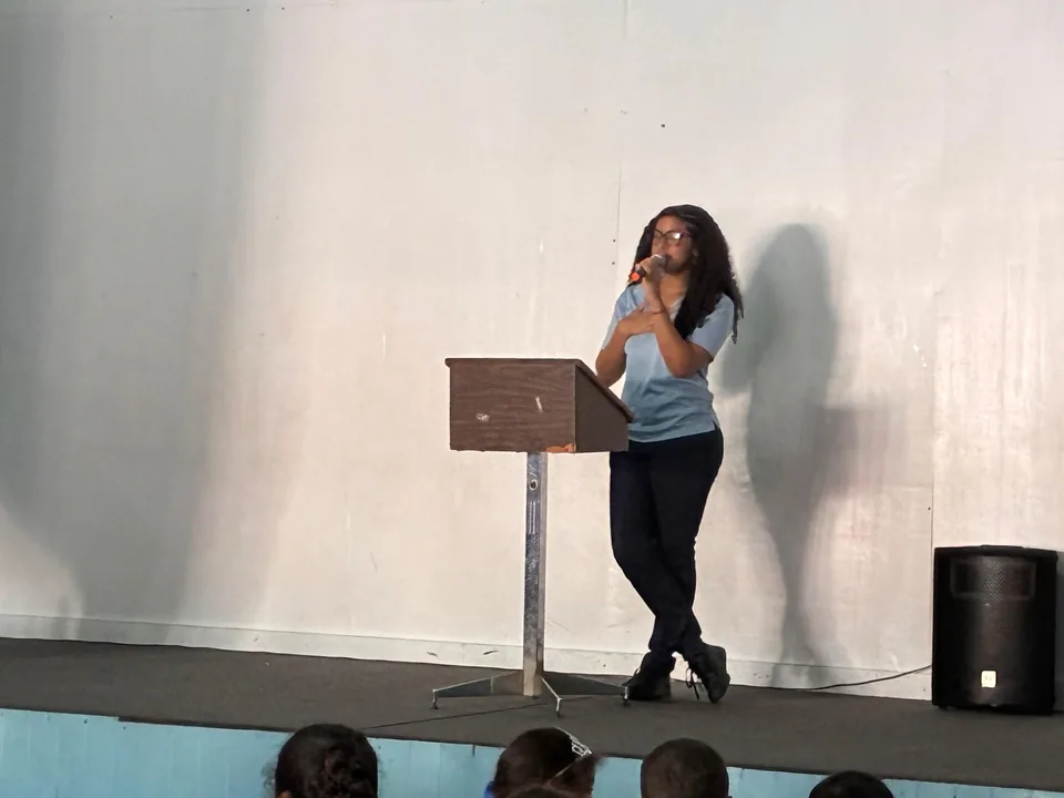 A student holds a microphone while addressing the audience beside the lectern