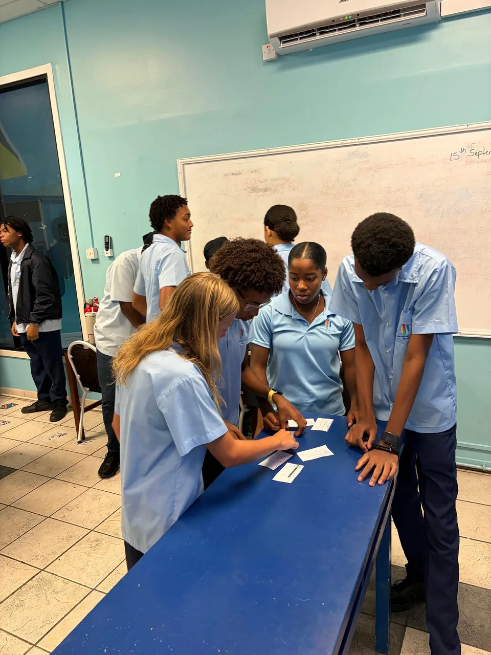 Students gather around a blue table arranging paper cards during a science activity