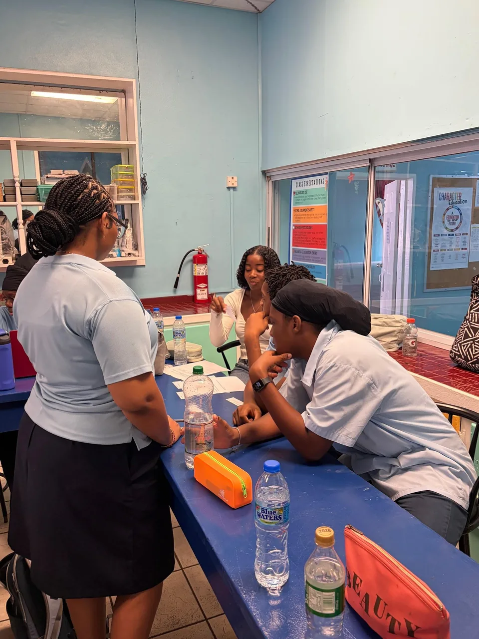 Students sit and stand around a table in the science room discussing their work