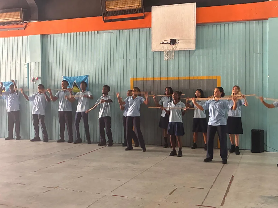 A line of students holding long sticks practise Kalinda movements in the hall