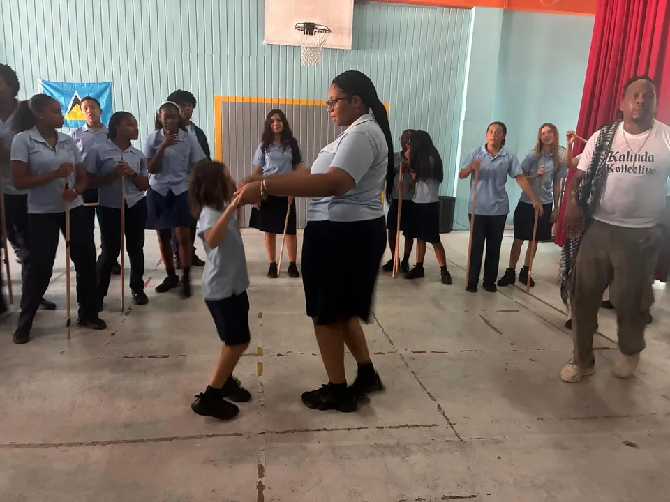 An older student dances with a young child while a Kalindeh Kollective member looks on