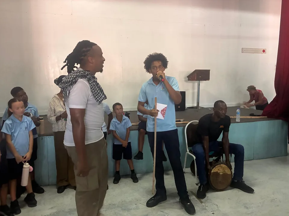 A facilitator and a student with a microphone perform for watching students, with a drummer behind them