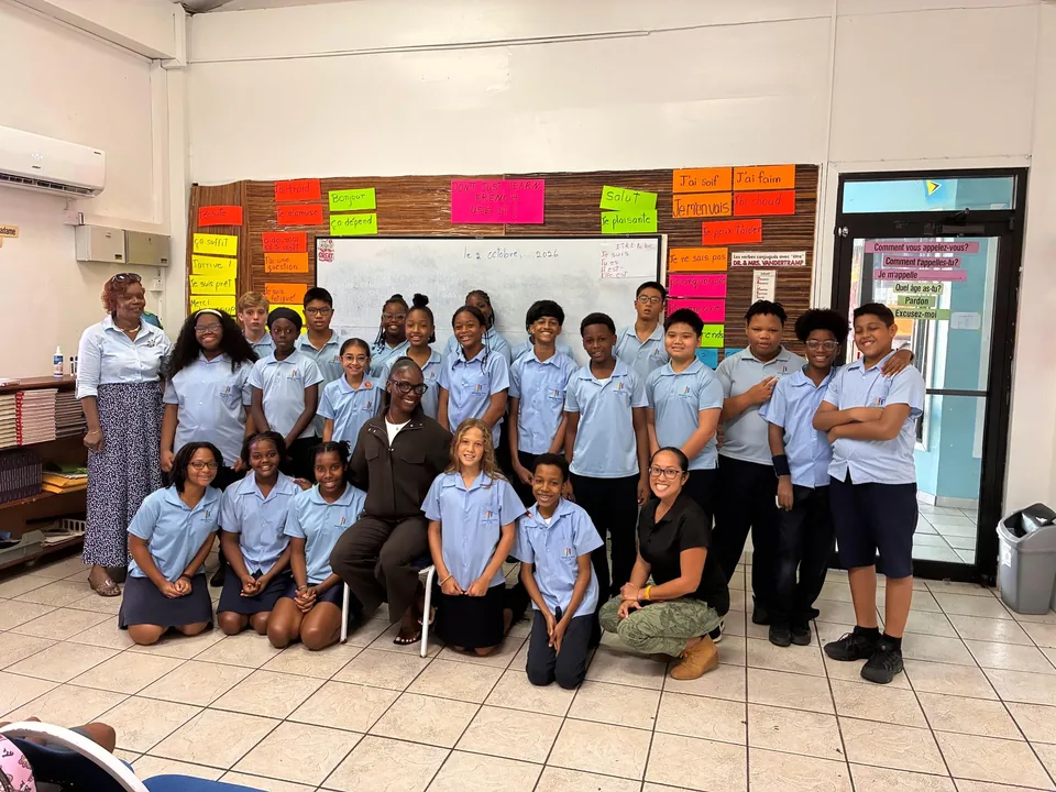 Julien Alfred kneels with a class in front of a colourful bulletin board