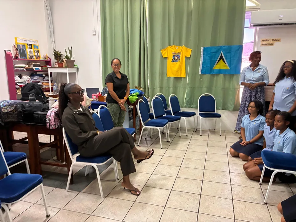 Julien Alfred sits and chats with students in a classroom beneath a Saint Lucia flag