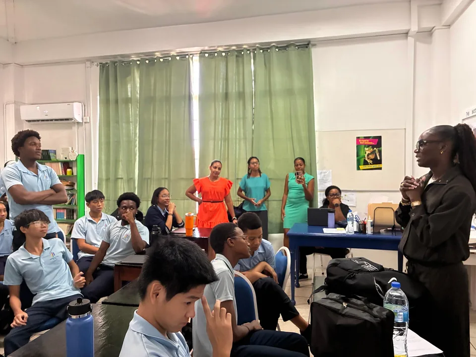 Julien Alfred speaks to a class of secondary students as staff look on