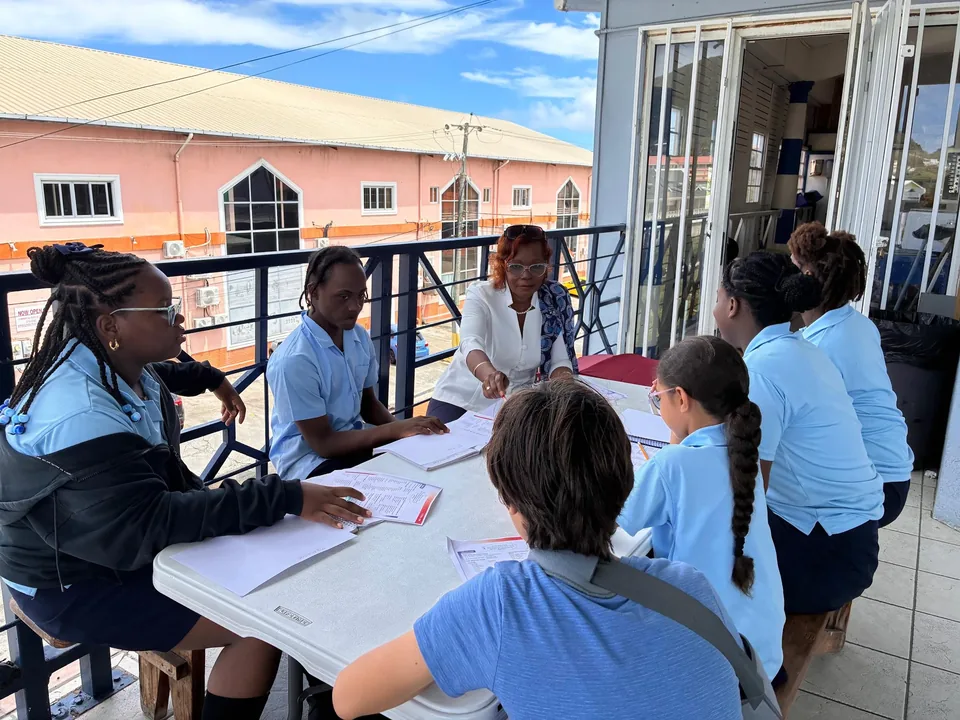 Students work on papers around a table on the school balcony with a teacher