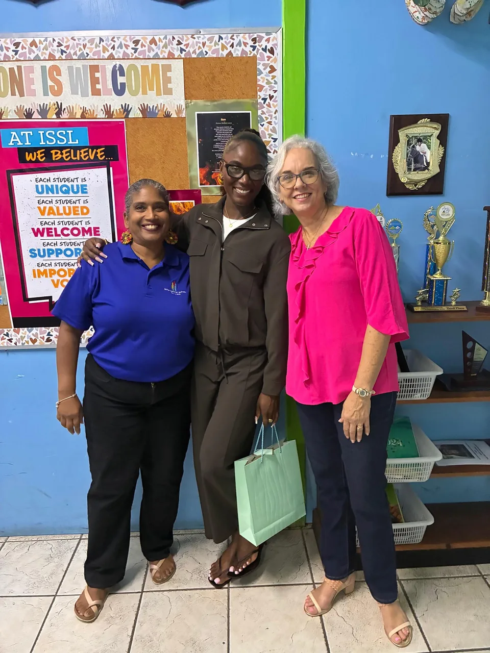Julien Alfred with two staff members beside the 'At ISSL we believe' board